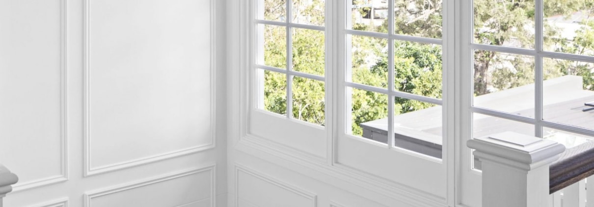 Freshly painted staircase in Brisbane home with white panelled walls, timber handrail and large windows