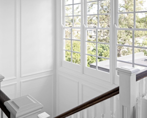 Freshly painted staircase in Brisbane home with white panelled walls, timber handrail and large windows